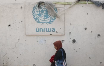 امرأة فلسطينية تسير أمام جدار متضرر يحمل شعار الأونروا في مخيم للنازحين برفح-وكالة الصحافة الفرنسية