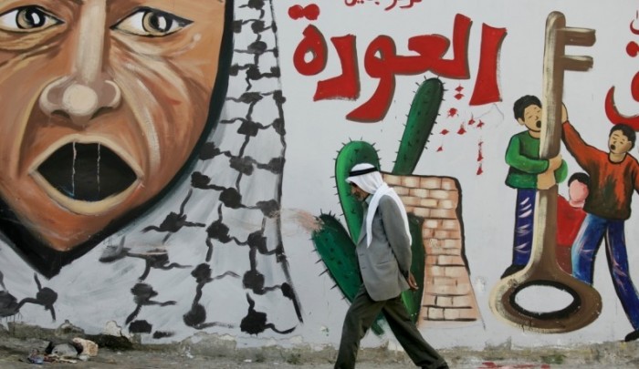 حاج فلسطيني يمشي أمام جدارية العودة في أحد المخيمات.jpg